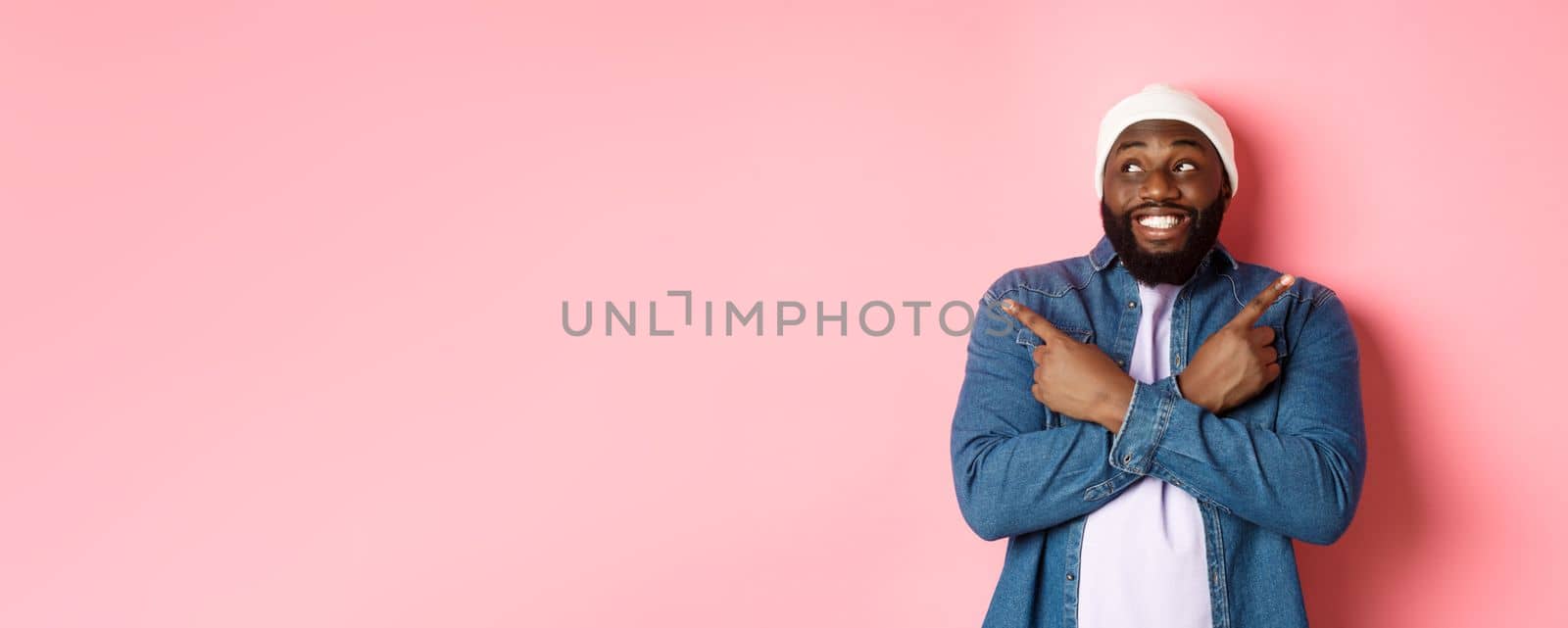 Excited young african-american man pointing sideways, showing two choices and making decision, smiling happy, standing over pink background.