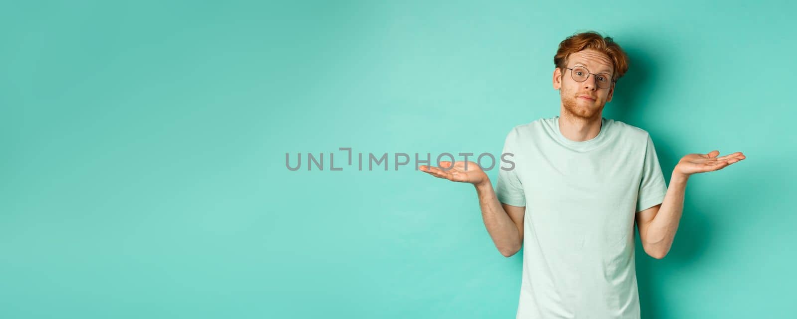 Portrait of confused redhead man in t-shirt and glasses know nothing, shrugging shoulders and looking clueless at camera, standing against turquoise background by Benzoix