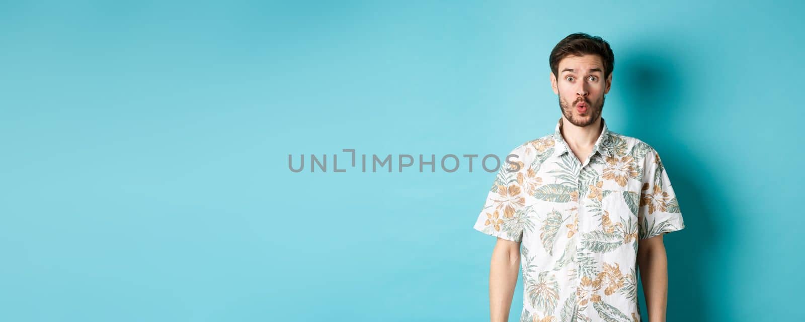 Summer holiday. Surprised tourist say wow and staring at camera, checking out awesome promo, standing in hawaiian shirt on blue background.