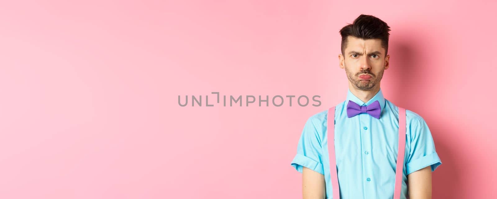 Sad and offended young man, frowning and pucker lips, looking angry at someone, standing disappointed against pink background in bow-tie by Benzoix