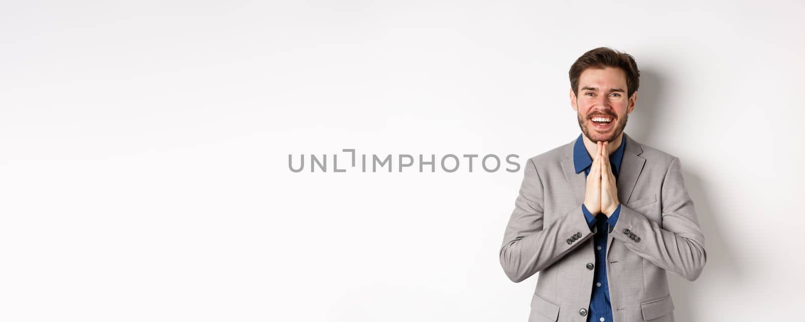 Happy caucasian businessman say thank you, smiling and laughing with hands showing namaste sign, express gratitude, standing on white background.