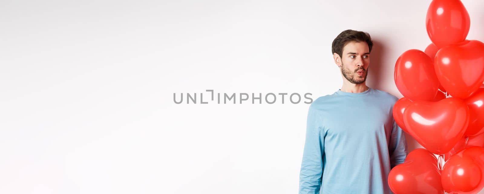 Relationship. Young man looking confused at heart balloon, puzzled on valetines day, standing over white background.