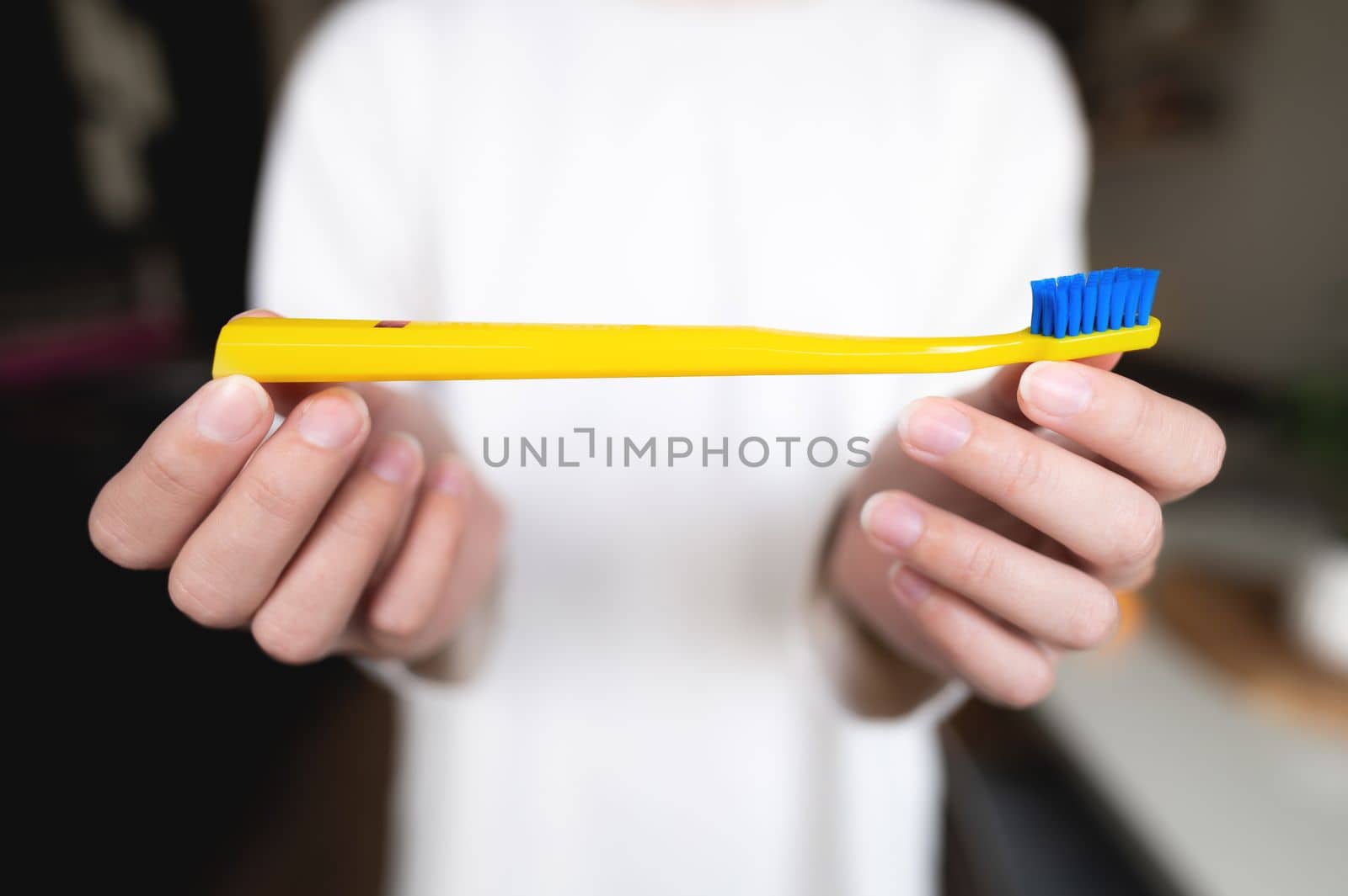 woman holds a bright toothbrush with two hands against the background of herself in a white sweater, the background is blurred by yanik88