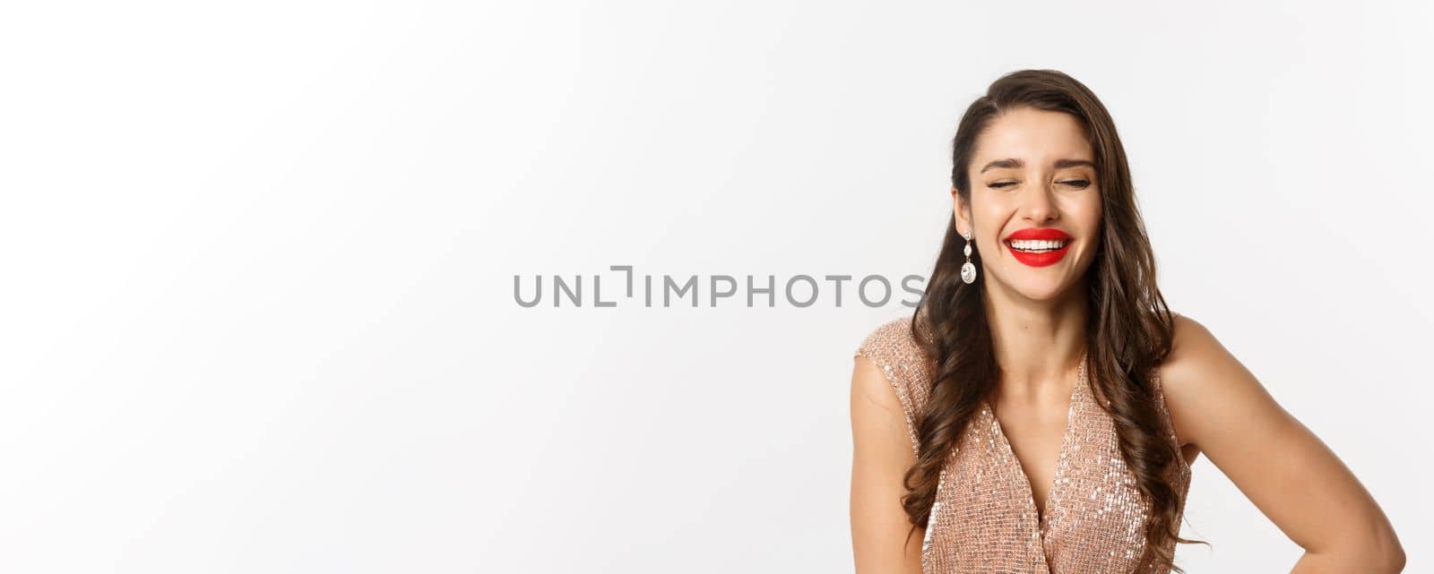 Concept of New Year celebration and winter holidays. Close-up of elegant woman in dress, with red lips, laughing and looking happy, standing over white background.