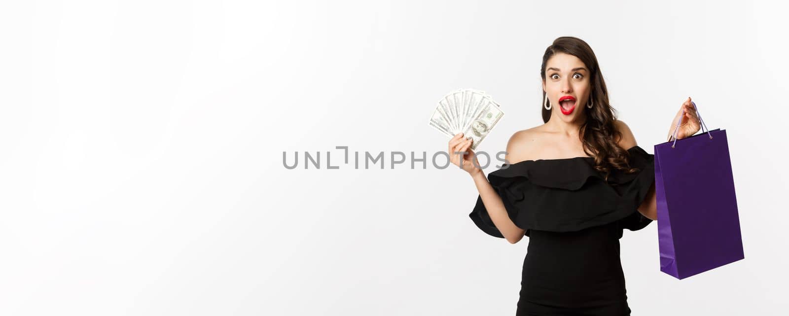 Happy woman buyer holding shopping bag and money, standing in black dress over white background by Benzoix