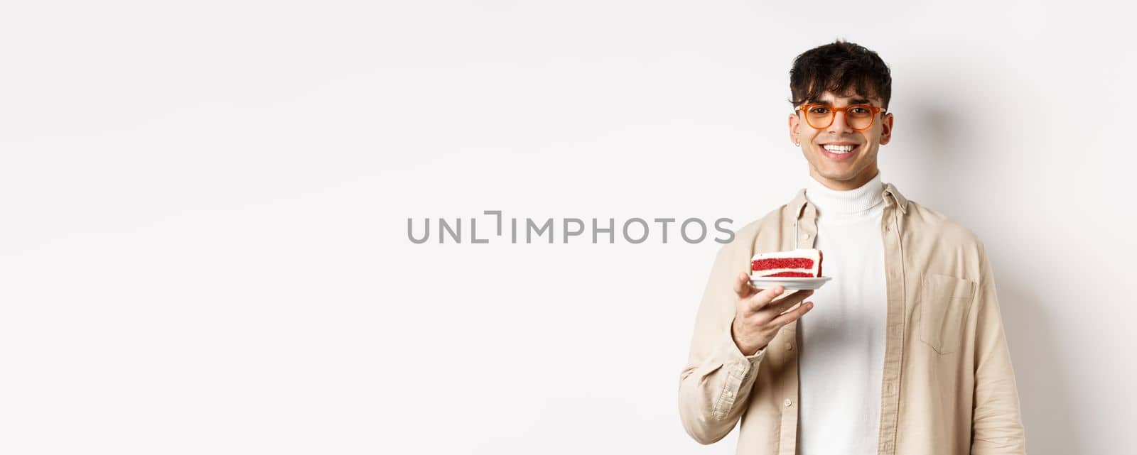 Happy caucasian guy celebrating birthday, holding cake with candle and smiling cheerful at camera, standing on white background by Benzoix