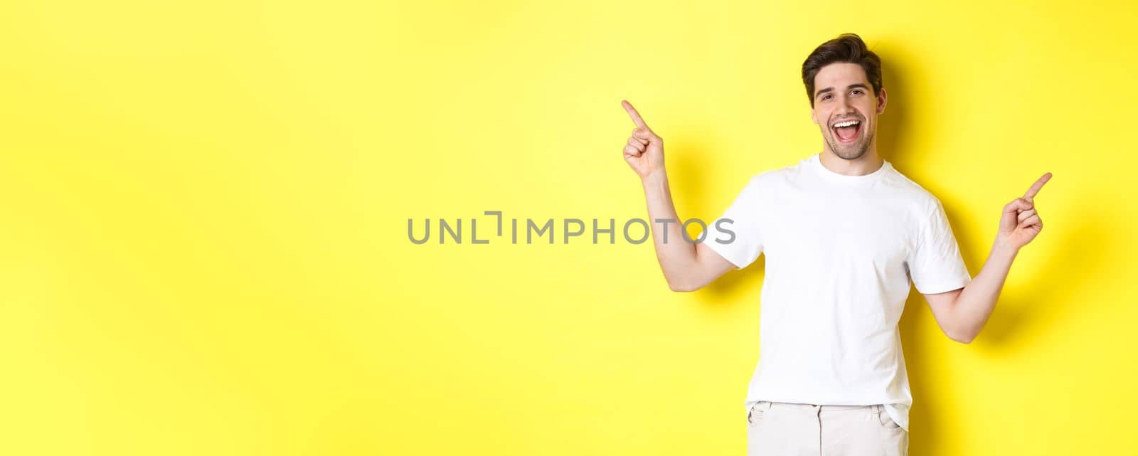 Happy stylish guy showing two variants, pointing fingers sideways at left and right promo, standing over yellow background by Benzoix