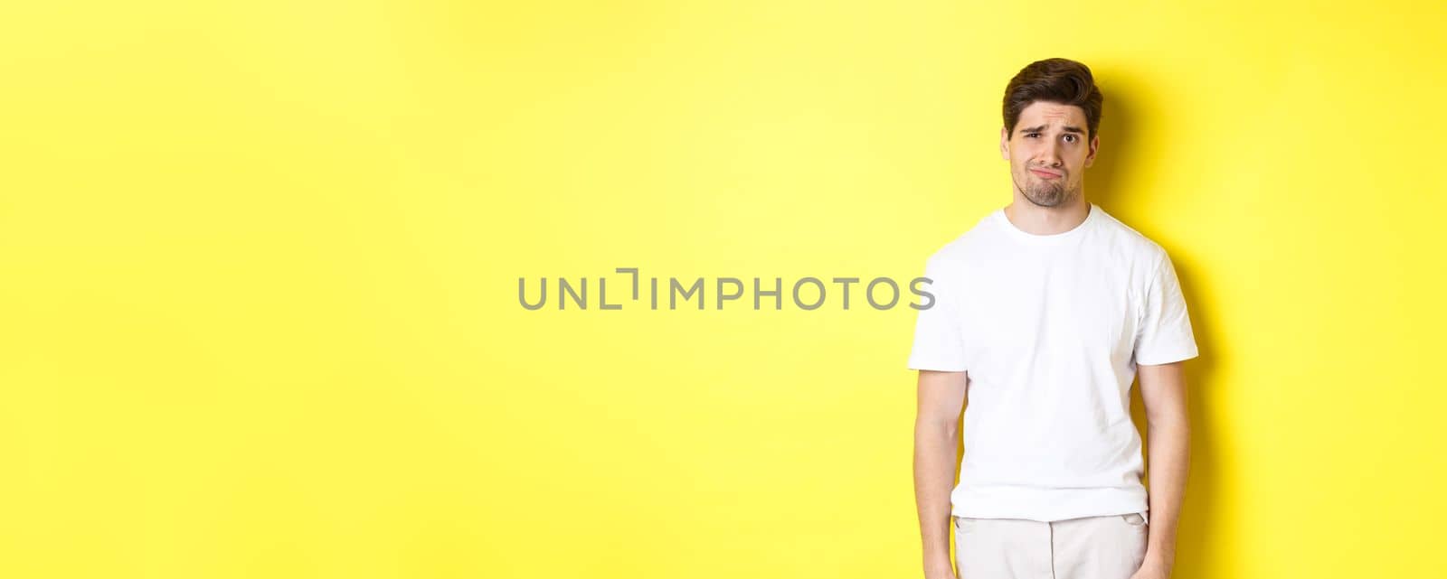 Disappointed guy looking upset, sulking and frowning, standing displeased against yellow background by Benzoix