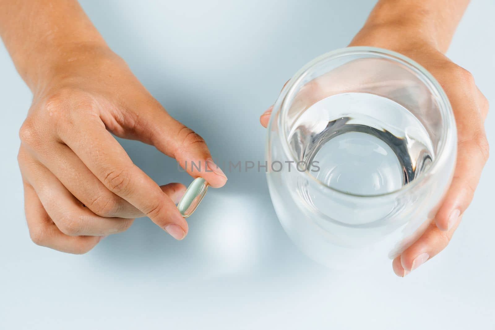 Omega 3 capsule of fish fat oil and cup of water in hands close-up. BADS pills of biologically active dietary supplements. Vitamin D for building and maintaining healthy bones. by Rabizo
