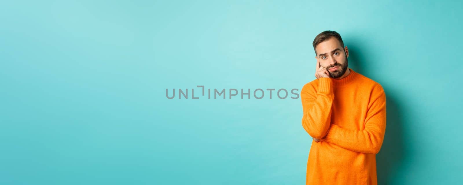 Sad and gloomy man with beard, looking indesicive and sad, thinking about something and sulking, standing over turquoise background by Benzoix