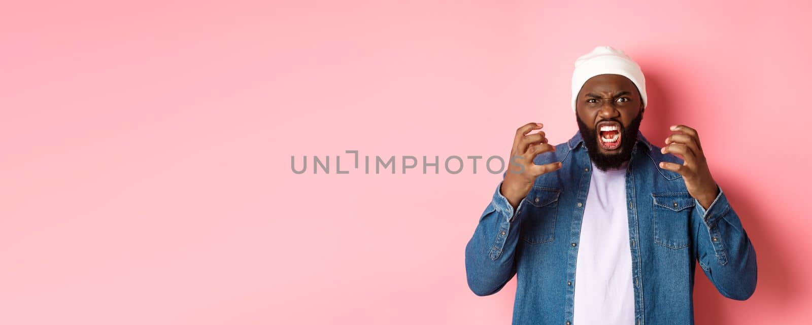 Angry african-american guy shouting and looking pissed-off, scream at camera, standing over pink background by Benzoix