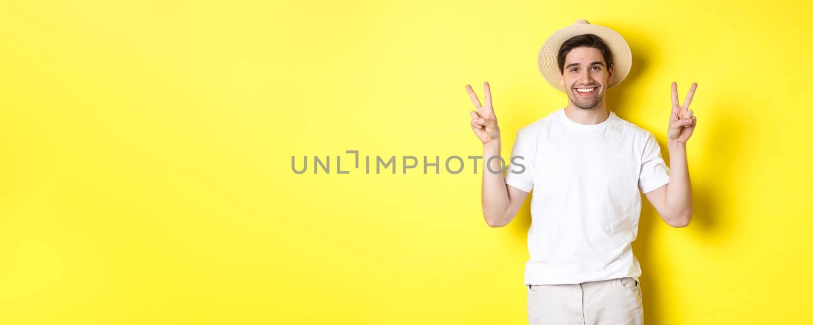 Concept of tourism and vacation. Happy male tourist posing for photo with peace signs, smiling excited, standing against yellow background.
