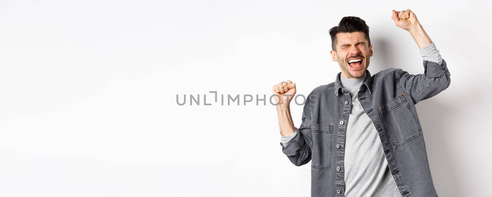 Sweet taste of success. Happy pleased young man screaming yes, making fist pump with pleased and relieved face, achieve goal and celebrating, triumphing as winning prize, white background.