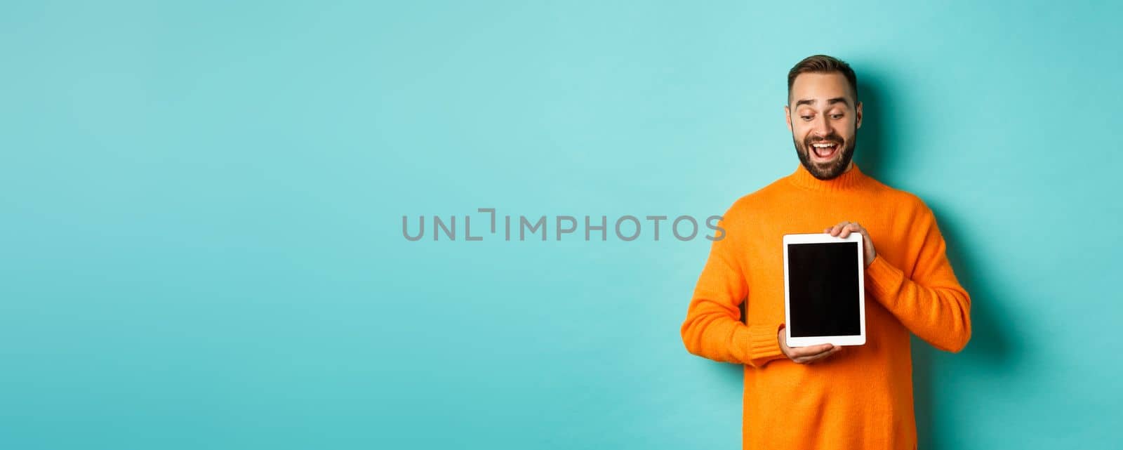 Technology. Cheerful adult man looking and showing digital tablet screen, standing over light blue background.