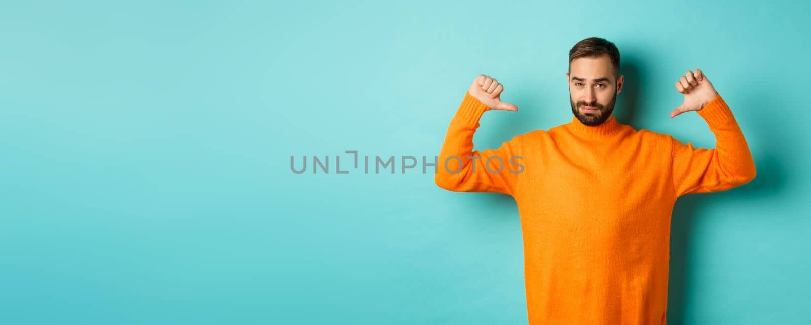 Confident attractive guy pointing at himself, show-off or brag, standing over light blue background.