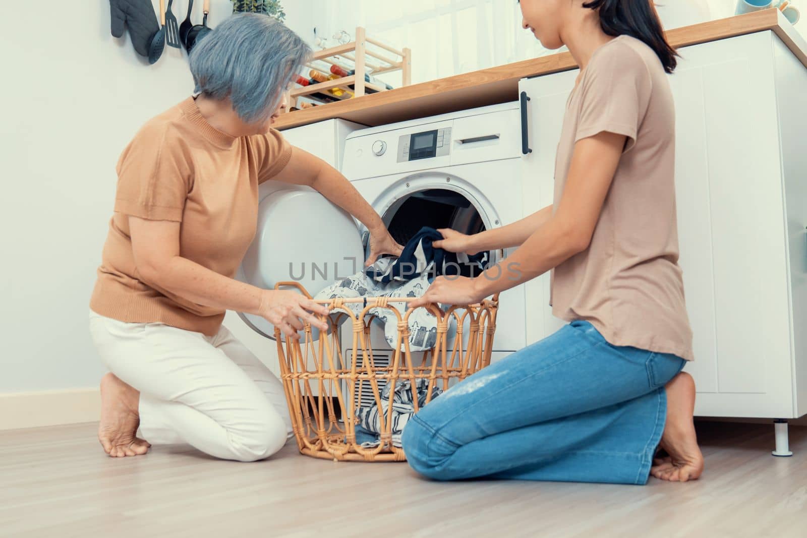 Daughter and mother working together to complete their household chores near the washing machine in a happy and contented manner. Mother and daughter doing the usual tasks in the house.