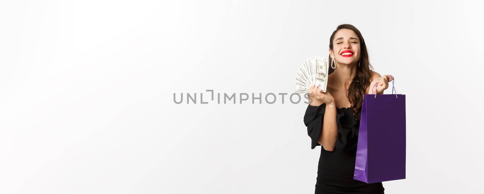 Satisfied and happy woman enjoying shopping, holding bag and money, smiling pleased, standing over white background.
