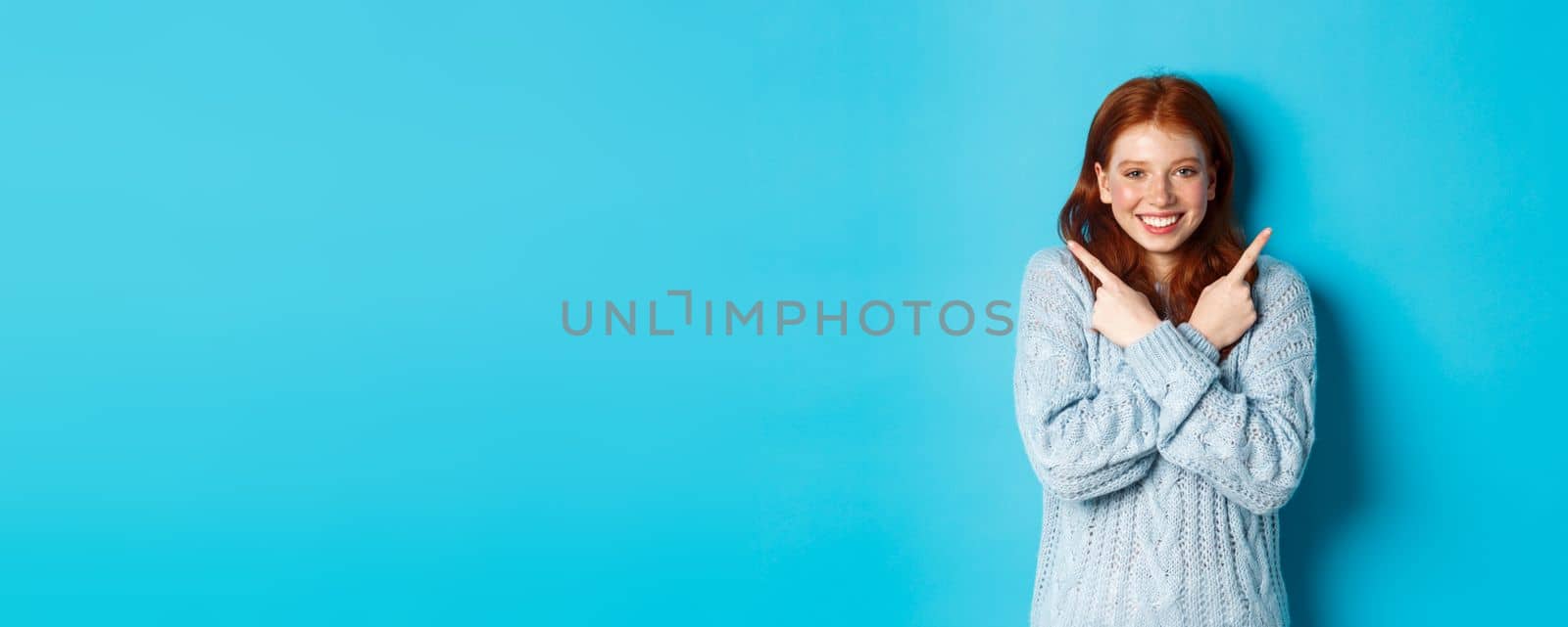 Cheerful redhead girl showing two choices, pointing sideways and smiling over blue background by Benzoix