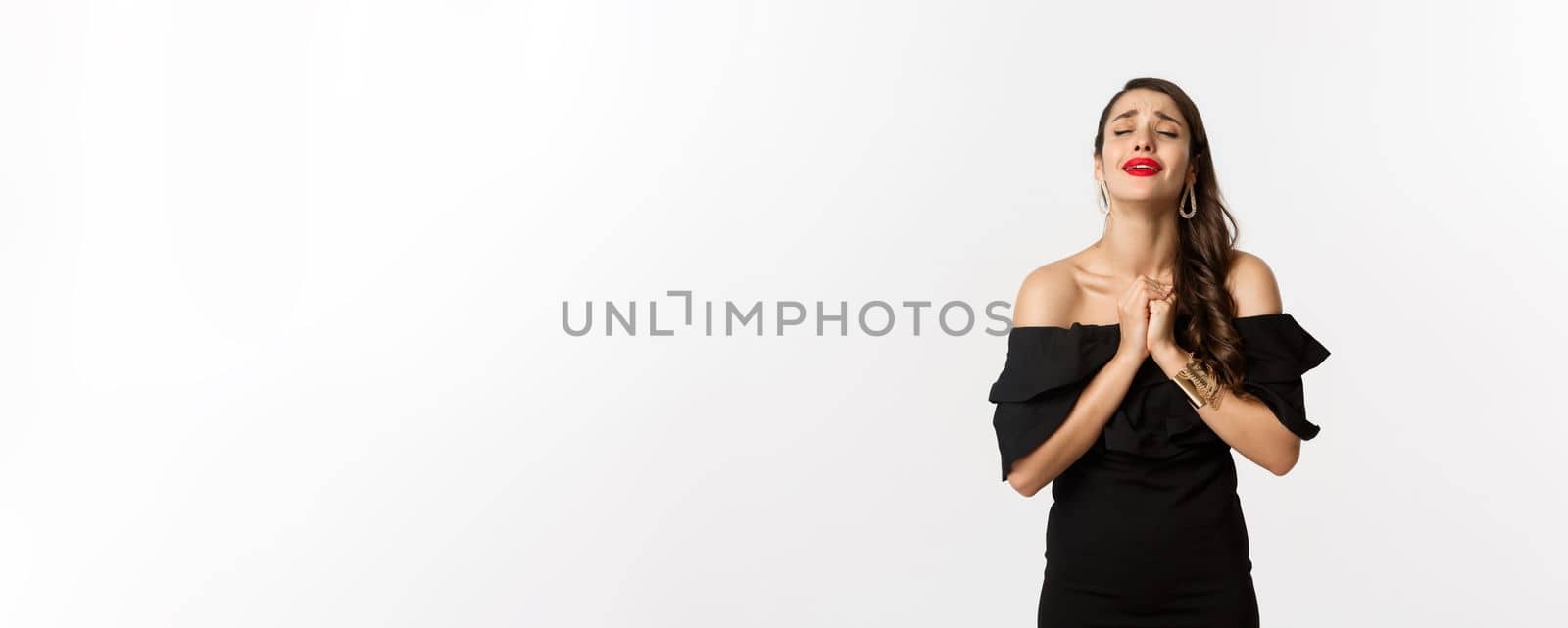 Fashion and beauty. Distressed brunette woman pleading, asking for help, praying while standing over white background.