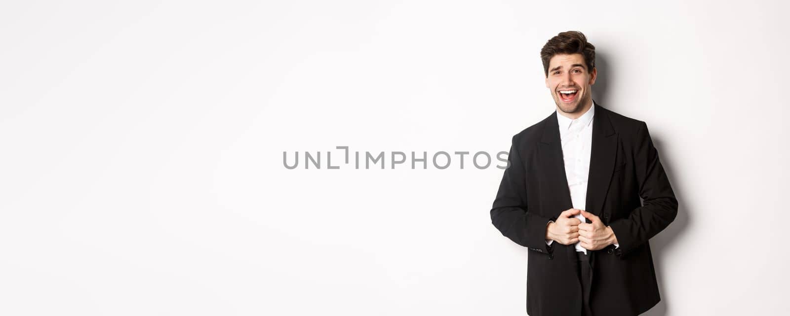 Concept of new year party, celebration and lifestyle. Portrait of handsome and confident man in suit, smiling pleased, feeling successful, standing over white background.