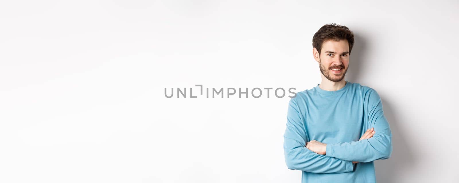 Confident young man with beard, cross arms on chest and smile at camera, standing like professional over white background.