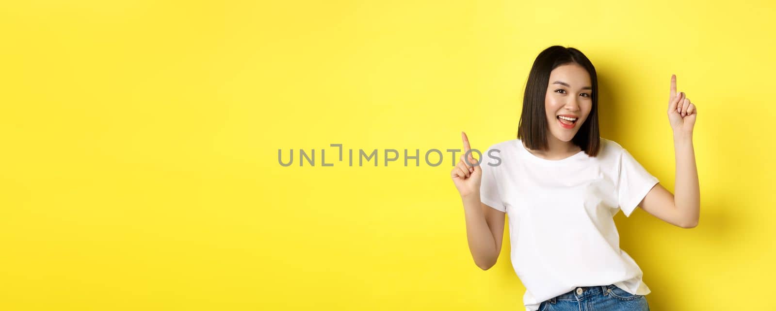 Happy asian woman dancing and having fun, posing in white t-shirt against yellow background.