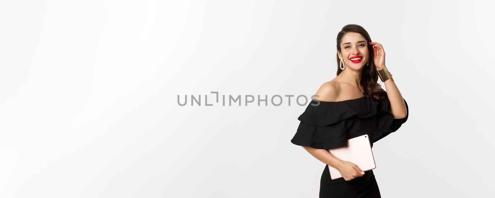 Fashion and shopping concept. Stylish young woman with glamour makeup, wearing black dress, holding digital tablet and smiling, white background by Benzoix