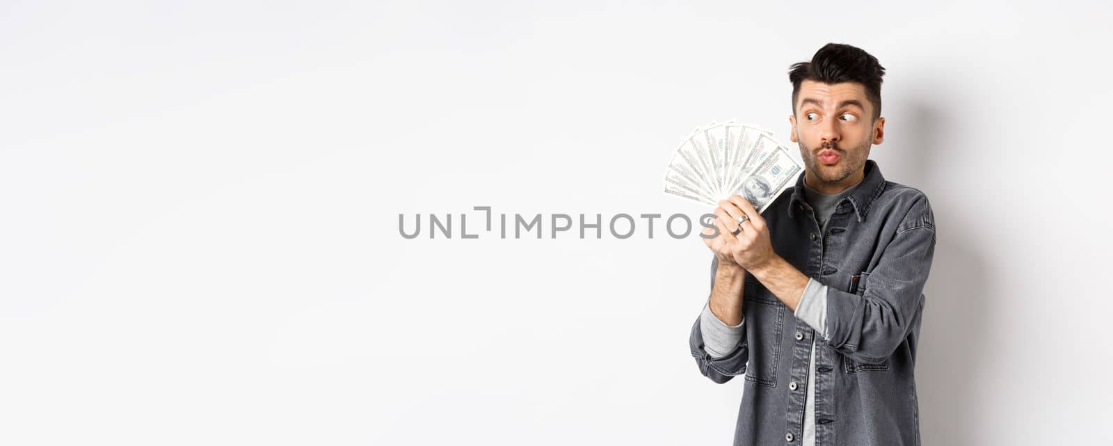 Excited man hugging and kissing dollar bills, holding money and rejoicing, standing on white background.