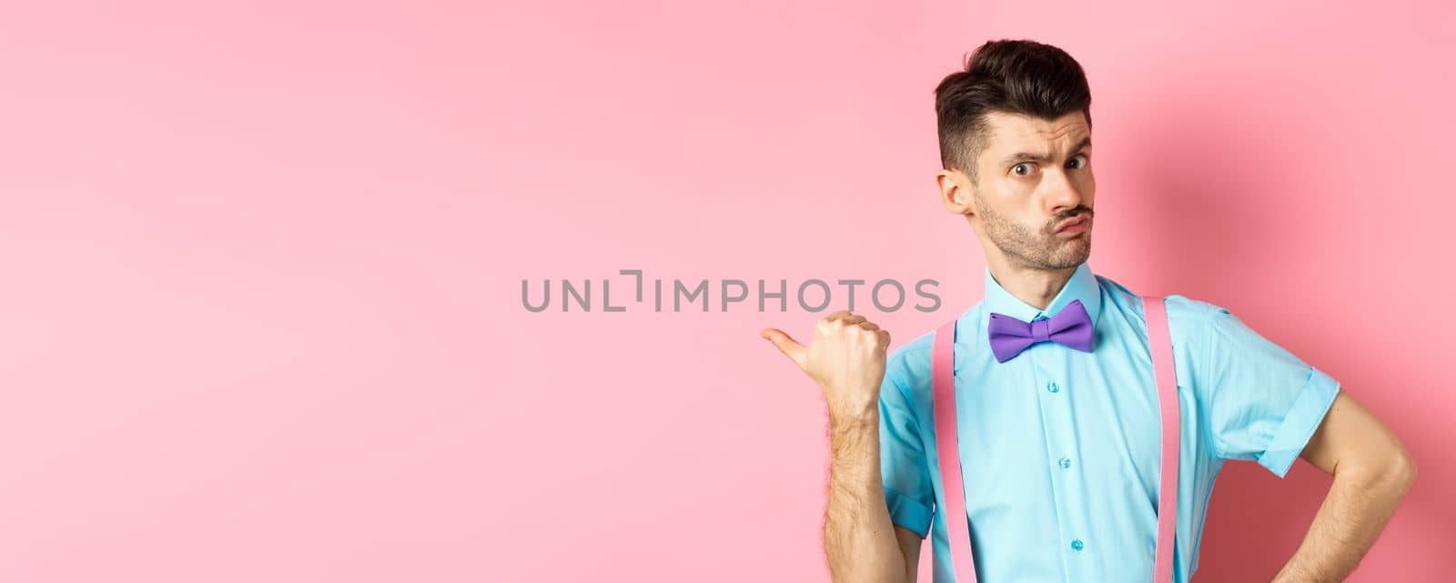 Serious-looking guy in suspenders suggessting to go outside, pointing left and looking confident at camera, starting fight, standing over pink background by Benzoix