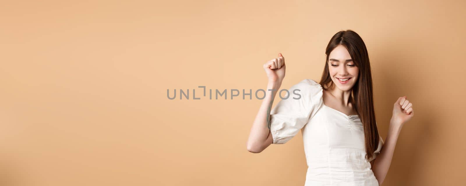 Carefree woman dancing and having fun, close eyes and smiling, standing on beige background by Benzoix