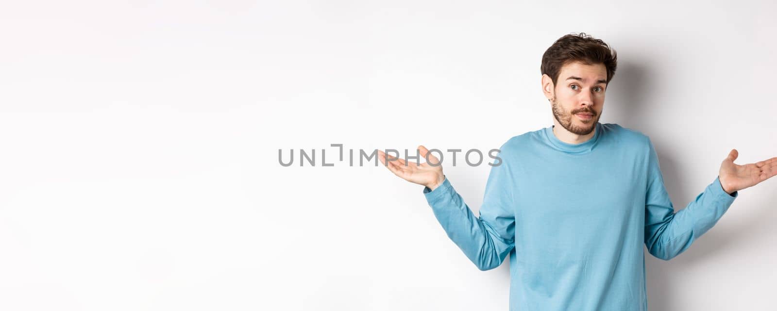 Clueless bearded guy in blue shirt, shrugging shoulders and looking unaware at camera, know nothing, standing on white background by Benzoix