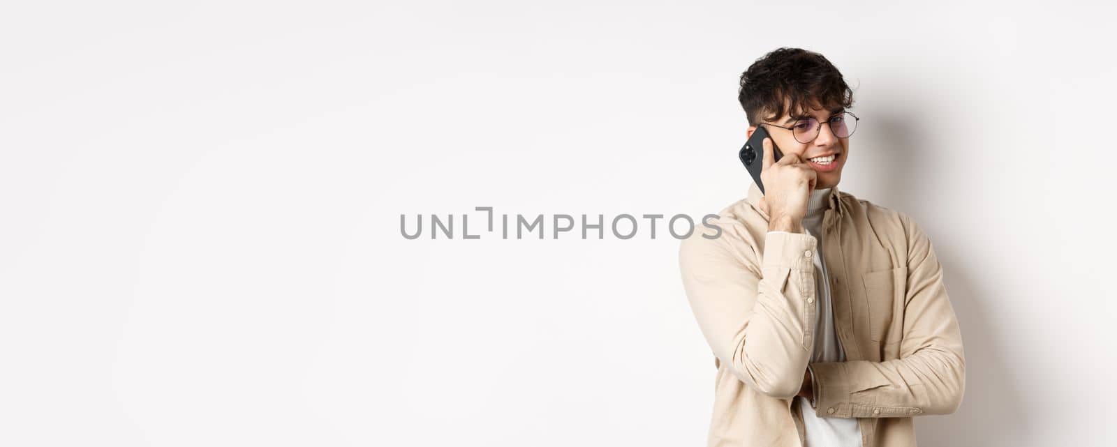 Real people concept. Handsome modern man talking on mobile phone, look aside and holding smartphone near ear, standing on white background.