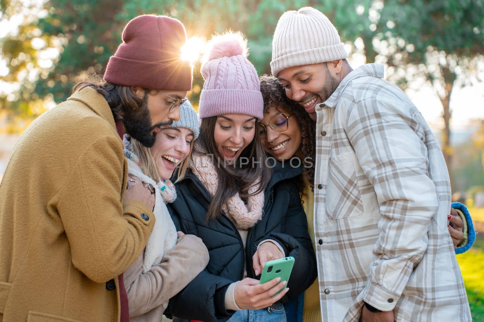 Big group of young multiracial friends looking cell phone excited happy smiling outdoors. Concept of millennial people addicted to technology. Social Media communication generation Z.