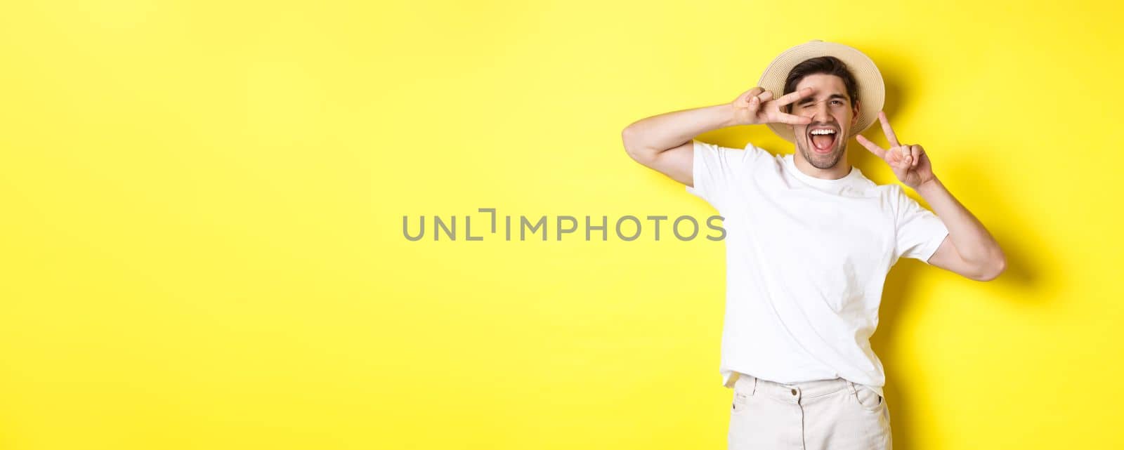 Concept of tourism and vacation. Happy man tourist posing for photo with peace signs, smiling excited, standing against yellow background by Benzoix