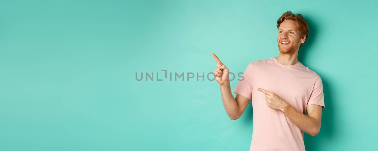 Handsome smiling man with red hair and beard looking delighted, pointing at upper left corner banner, standing in t-shirt over mint background by Benzoix