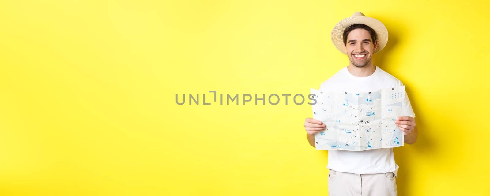 Travelling, vacation and tourism concept. Smiling young man going on trip, holding road map and smiling, standing over yellow background by Benzoix