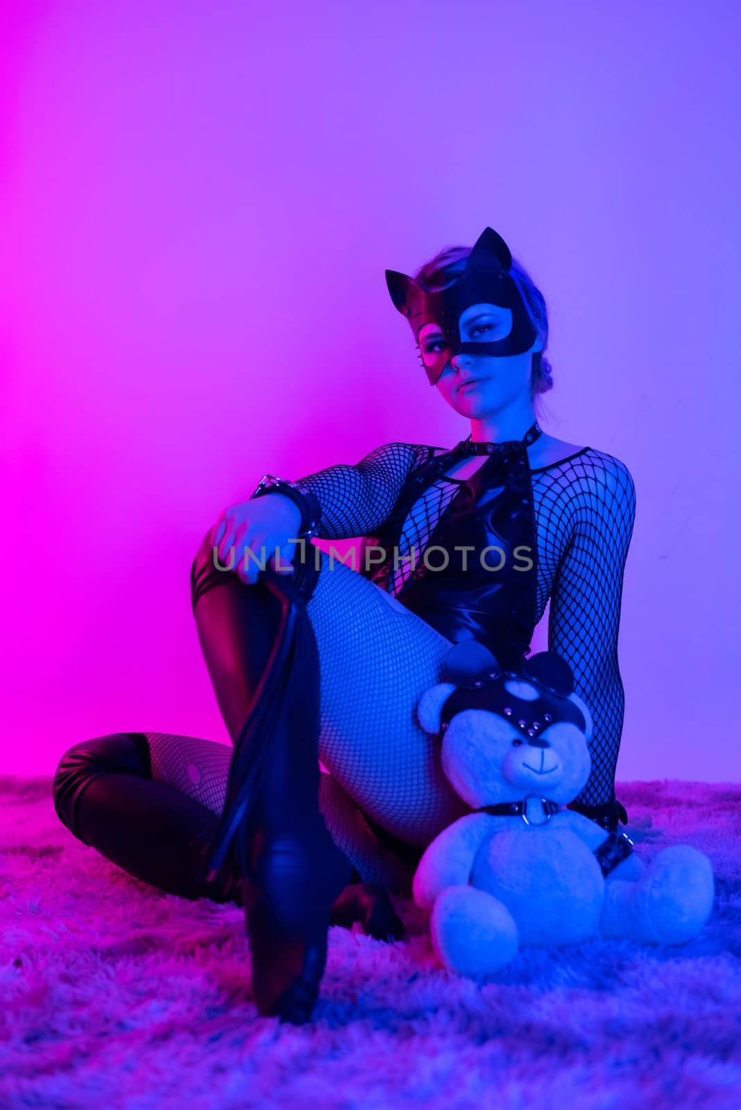 sexy girl in costume and mask bdsm games in neon light with empty background