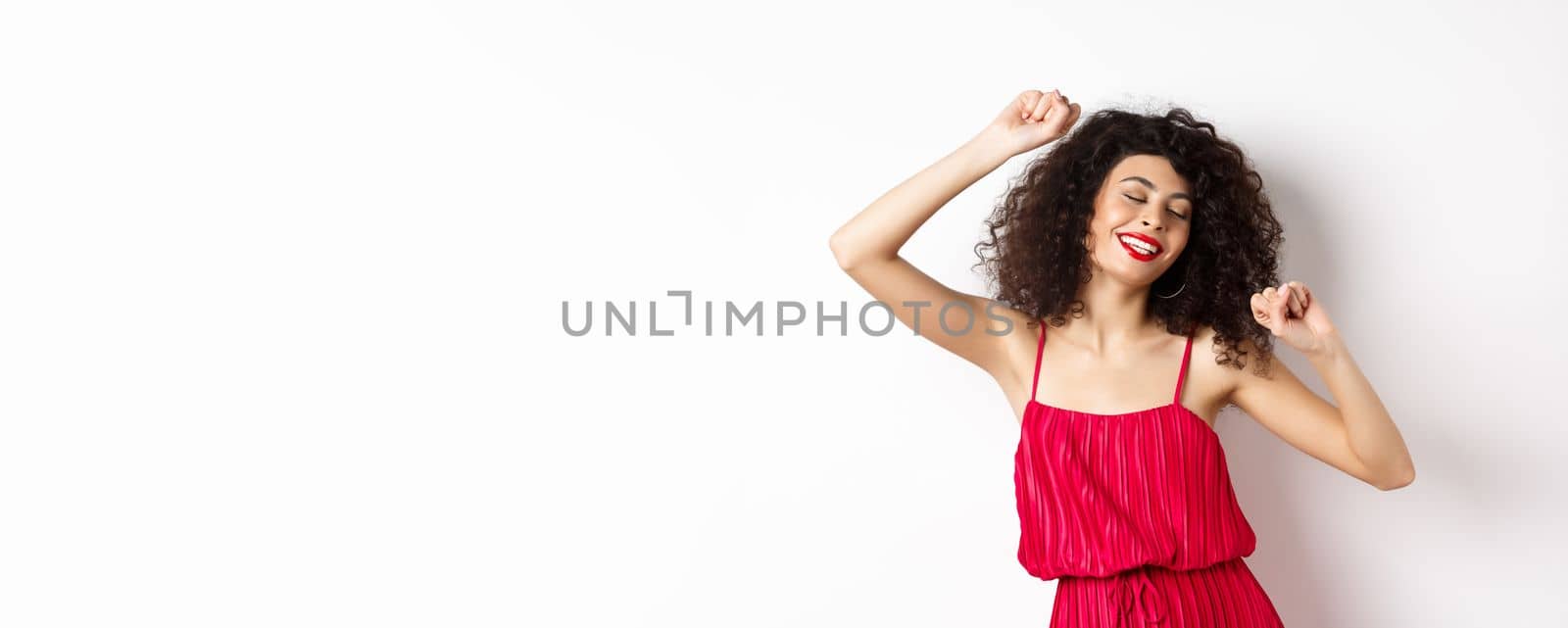 Happy elegant woman in red dress dancing on white studio background.