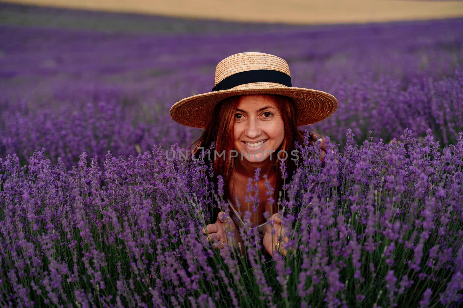 Close up portrait of a happy young woman in a dress on blooming fragrant lavender fields with endless rows. Bushes of lavender purple fragrant flowers on lavender fields