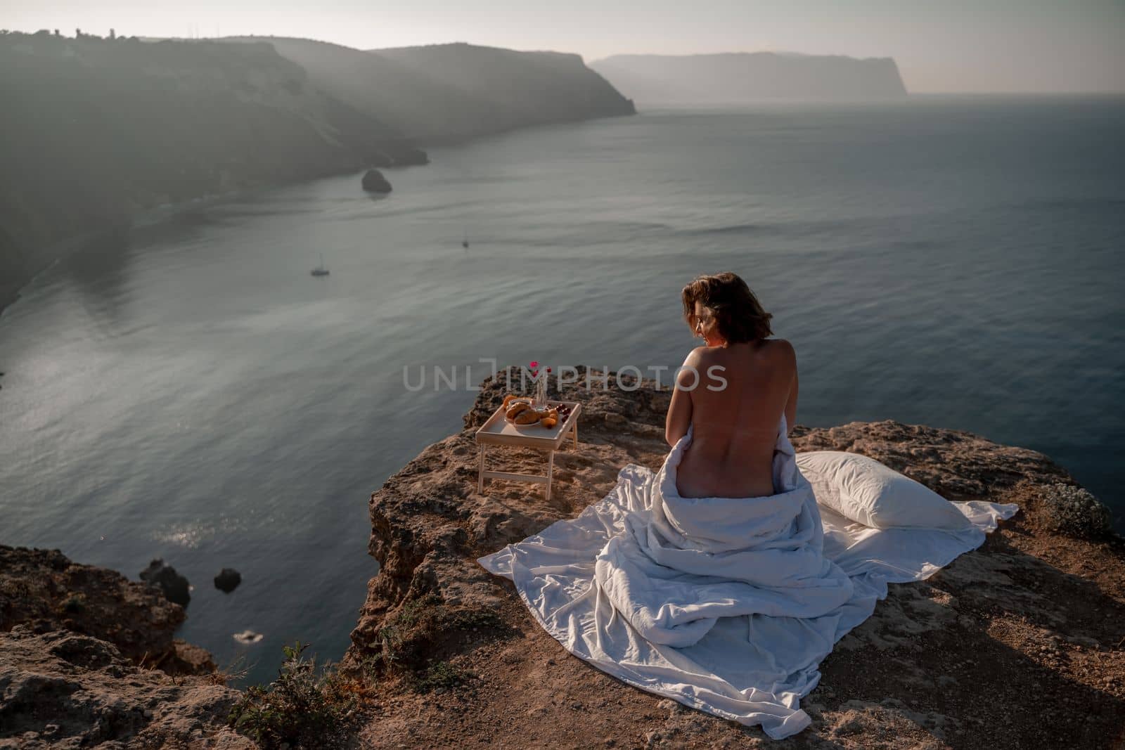 Woman wake up in bed wuth duvet and pillow over nature sea background outdoors. Back view. Good morning. Freedom concept