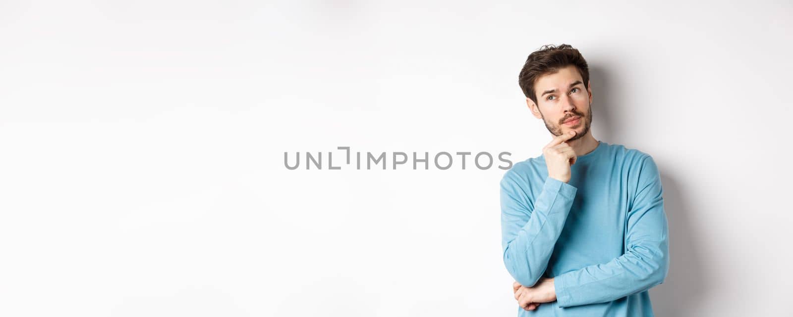 Image of handsome young man making choice, thinking and looking pensive up, standing over white background by Benzoix