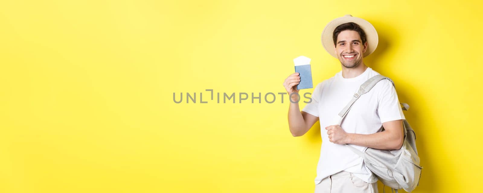 Tourism and vacation. Smiling young guy going on trip, holding backpack and showing passport with tickets, standing over yellow background.