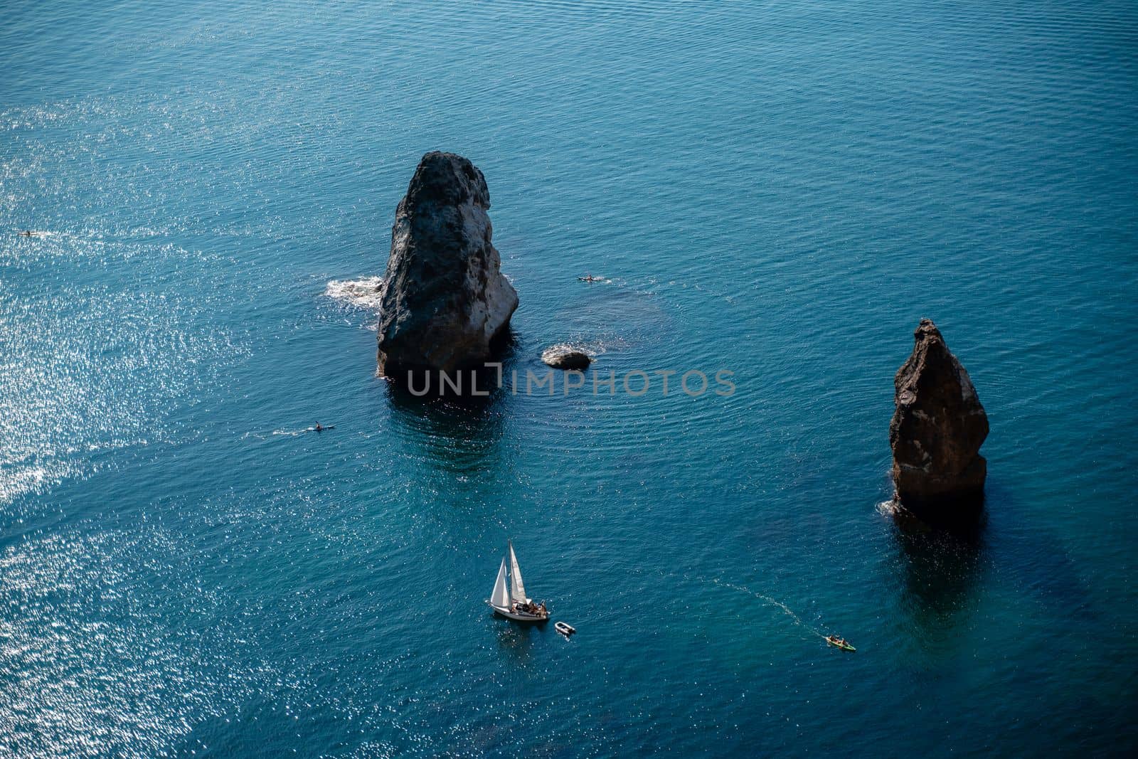 Two rocks stick out of the water in the middle of the turquoise sea. Scenic ocean view. Speed boat sails on the sea. High quality photo.