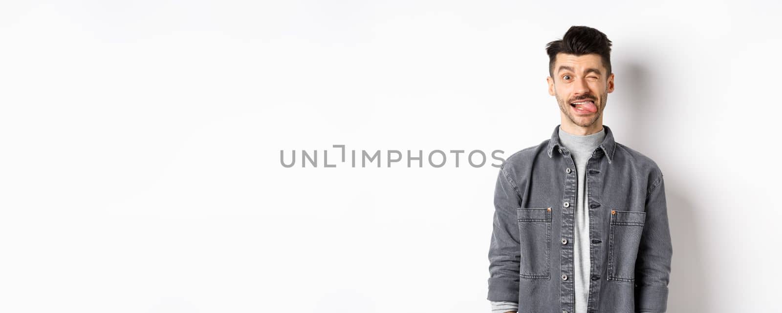 Funny guy with moustache showing tongue and winking, making you laugh, standing on white background.