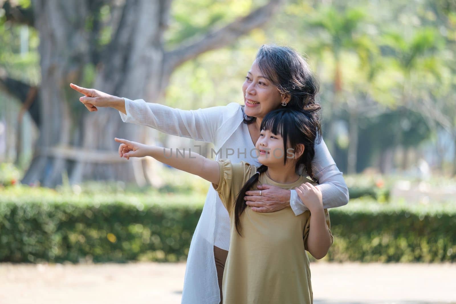 Asian Grandmother and Granddaughter hug together outdoor park. Hobbies and leisure, lifestyle, family life, happiness moment concept.