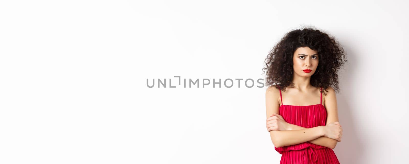 Sad and offended caucasian woman in red dress frowning, cross arms on chest and sulking, feeling mad at you, standing over white background by Benzoix