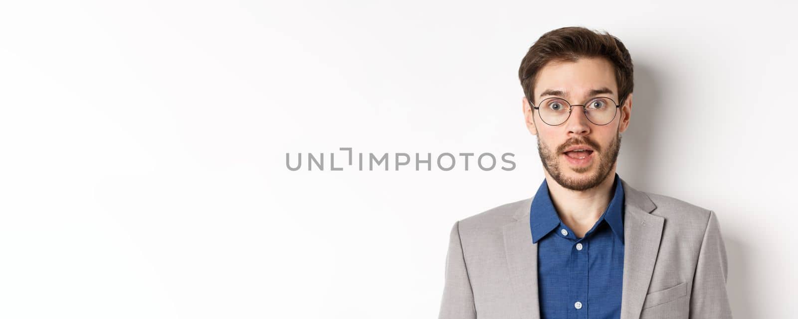 Close-up of surprised business man in glasses and suit gasping amazed, hear good news, standing on white background.