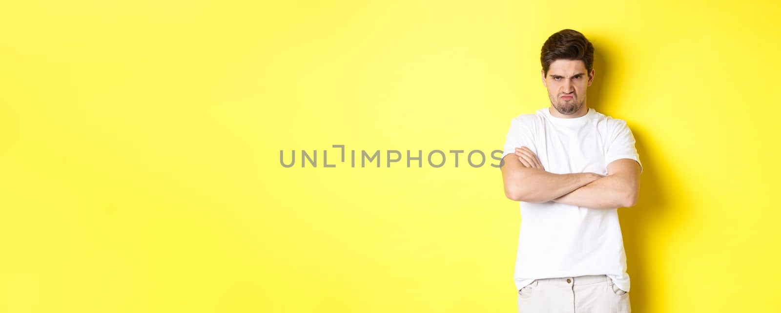 Offended and mad guy, frowning and sulking, holding hands crossed on chest, standing angry against yellow background by Benzoix