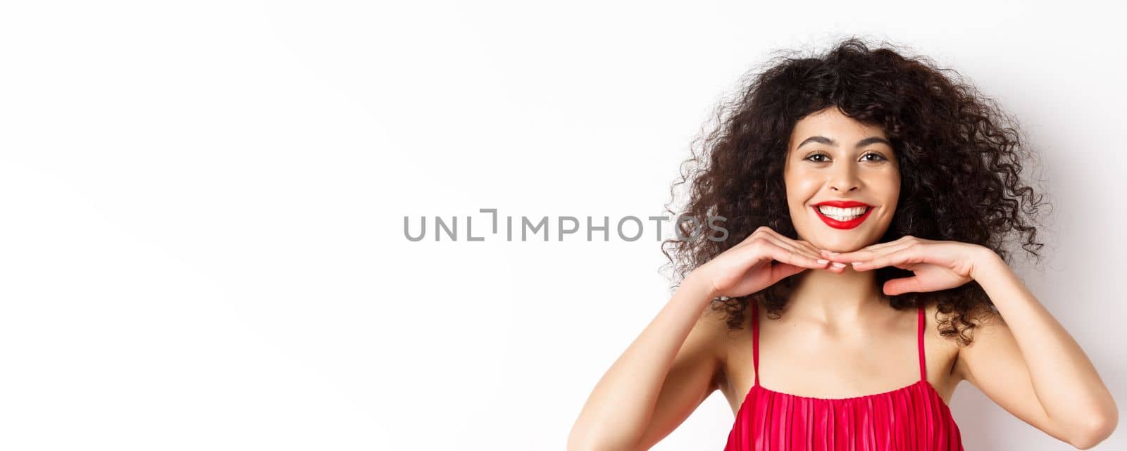 Beauty and makeup. Pretty lady with curly hair, red lips and white teeth, smiling and showing perfect face, standing on white background.