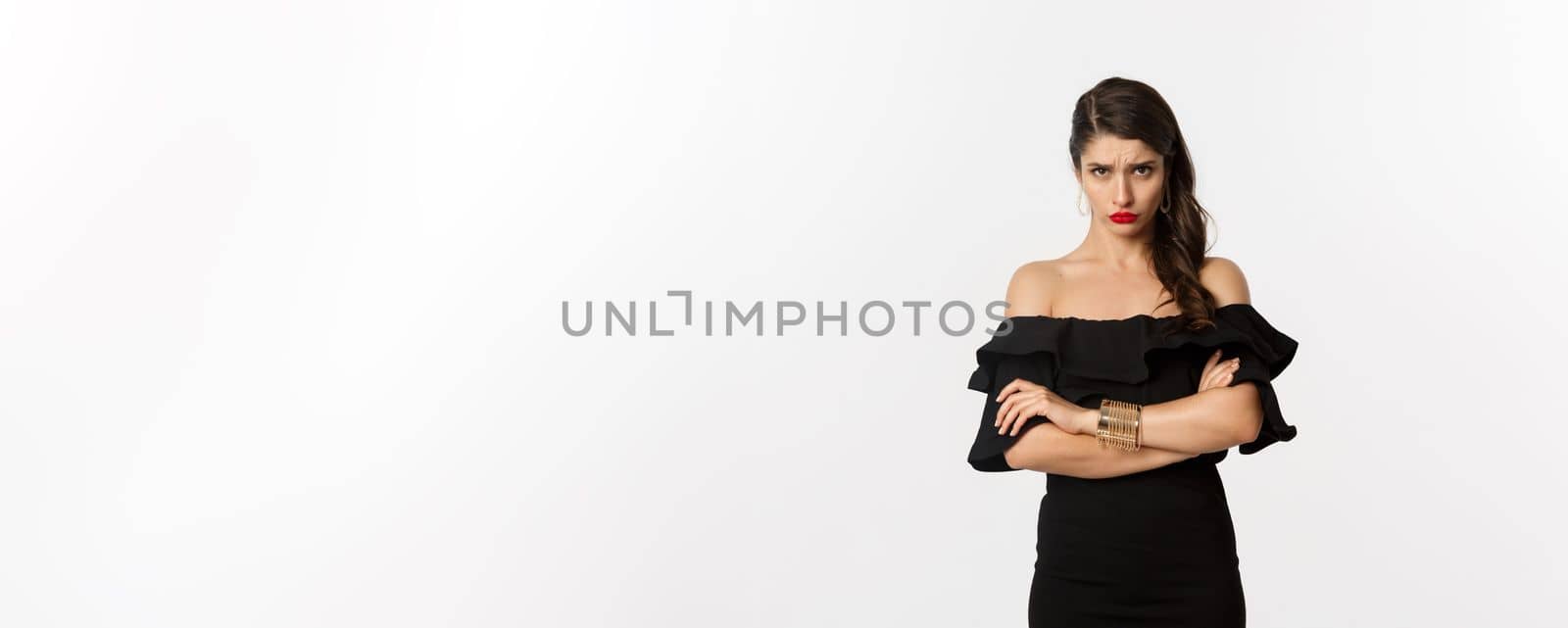 Fashion and beauty. Cute sulking girlfriend feeling offended, looking from under forehead with arms crossed, angry at person, standing over white background.